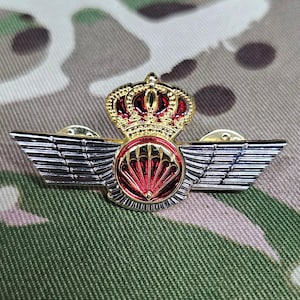 May include: A gold and silver pin with a red parachute and a crown. The pin is a military insignia.