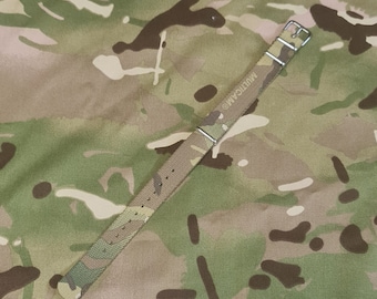 May include: A brown, green, and tan camouflage watch strap with a silver buckle. The strap is labeled "MULTICAM".