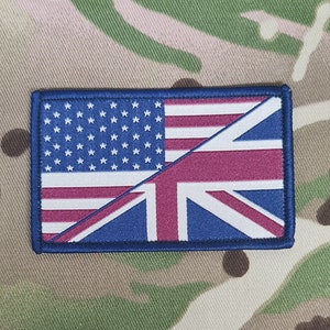 Może przedstawiać: Niebieska łatka z amerykańską i brytyjską flagą zszytymi razem po przekątnej. Flaga amerykańska znajduje się po lewej stronie, a flaga brytyjska po prawej. Obie flagi są czerwono-biało-niebieskie.