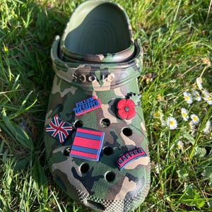 May include: Camouflage Crocs with various charms, including a red poppy, a Union Jack flag, a red and blue striped charm, and a blue charm with the text "Follow the Sapper" and "Sapper".