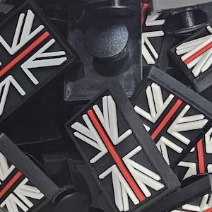 Può includere: Toppe rettangolari nere con il design della Union Jack. Il design incorpora linee diagonali bianche, una linea rossa centrale e uno sfondo nero. Le toppe sono sparse e sovrapposte.