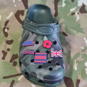 Peut inclure: Sabot vert camouflage avec divers charmes de chaussures colorés. Les charmes comprennent un coquelicot rouge, un charme rayé bleu et rouge, un charme bleu avec le texte "SAPPER" et un charme bleu avec le texte "FOLLOW THE SAPPER". Le sabot a également un charme bleu avec un drapeau de l'Union Jack.