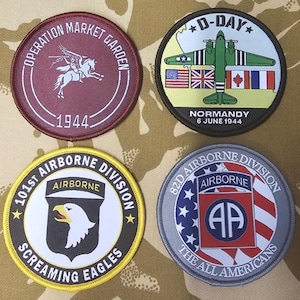 Puede incluir: Cuatro parches redondos bordados con temas militares. Uno presenta un caballo alado y el texto "OPERATION MARKET GARDEN 1944". Otro muestra un avión verde con banderas y "D-DAY NORMANDY 6 JUNE 1944". Los otros muestran águilas y banderas.