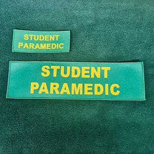 Könnte beinhalten: Zwei rechteckige grüne Patches mit gelbem Text, der "STUDENT PARAMEDIC" lautet.