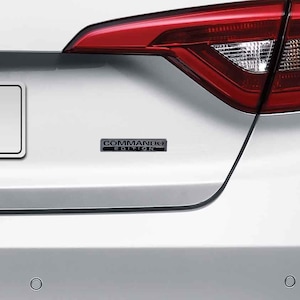 May include: A white car with a black "COMMAND EDITION" emblem on the back.
