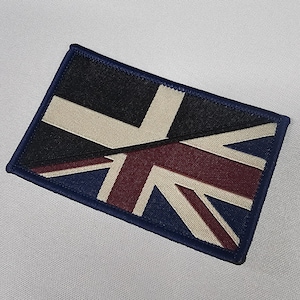 Peut inclure: Écusson rectangulaire avec un motif Union Jack. L'écusson a une bordure bleu marine et présente des couleurs noir, beige, bordeaux et bleu marine. Le motif est une représentation du drapeau du Royaume-Uni.