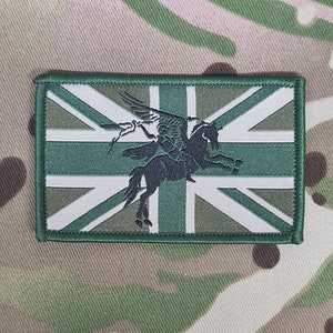 Peut inclure: Un écusson brodé avec un motif Union Jack en vert et blanc et une silhouette noire d'un cavalier sur un cheval ailé.