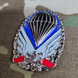 May include: A silver metal pin with a blue, white, and black parachute design. The pin features a red and white ribbon with a silver eagle design.