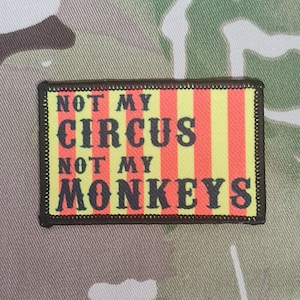 Può includere: Una toppa ricamata nera e gialla con il testo "Not My Circus Not My Monkeys" su uno sfondo a strisce rosso e giallo.