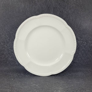 May include: A white ceramic dinner plate with a scalloped edge and a beaded rim.