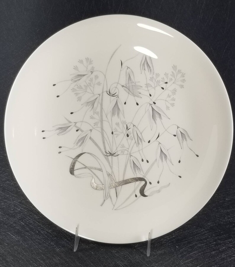May include: A white ceramic dinner plate with a silver floral design. The design features a bouquet of stylized flowers and leaves.