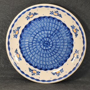 May include: A white ceramic plate with a blue and white floral design. The plate has a scalloped edge and a blue and white border.