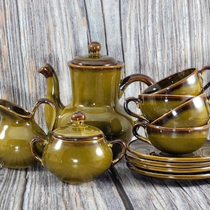May include: A brown and green ceramic tea set with a teapot, creamer, sugar bowl, four cups, and four saucers.
