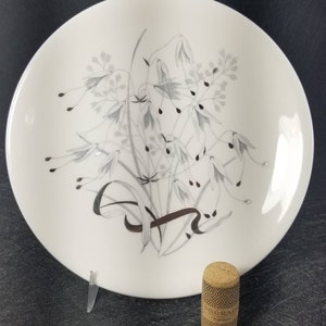 May include: A white ceramic dinner plate with a silver and gray floral design. The plate has a simple, elegant design.