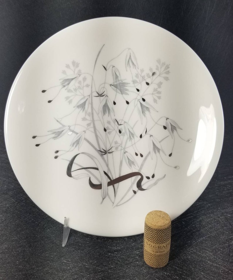 May include: A white ceramic dinner plate with a silver and gray floral design. The plate has a simple, elegant design.