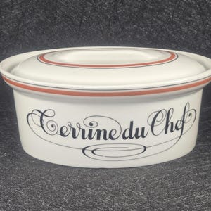 May include: White ceramic terrine with a lid, featuring a red and black trim. The words "Terrine du Chef" are elegantly scripted on the front. A classic piece for serving and storing food.
