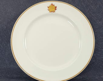 May include: White ceramic plate with a gold rim and a logo in the center that reads "Canadian National Hotels". The logo features a stylized maple leaf in red, orange, and yellow.
