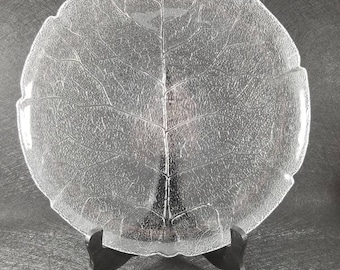 May include: A clear glass plate with a leaf design. The plate is on a black stand.