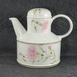 May include: White ceramic teapot with a floral design featuring pink carnations and green leaves. The teapot has a round body and a lid with a small hole in the top.