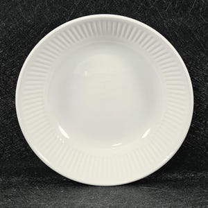 May include: A round white ceramic bowl featuring a smooth, deep centre basin and a wide, flat rim decorated with a series of evenly spaced, vertical embossed ridges that extend around the entire circumference of the plate's edge.