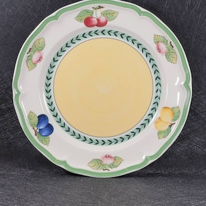 May include: A white ceramic dinner plate with a green and yellow border. The plate features a floral design with cherries, plums, and lemons.
