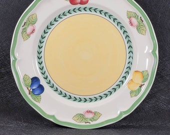 May include: A white ceramic dinner plate with a green and yellow border. The plate features a floral design with cherries, plums, and lemons.