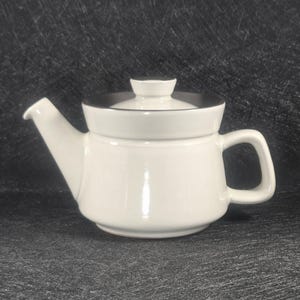 May include: A white ceramic teapot with a black rim on the lid and a matching handle. The teapot has a spout for pouring and a small knob on the lid. The design is simple and elegant, suitable for serving tea.