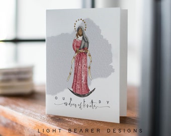 May include: A watercolor illustration of Our Lady of Knots, a Catholic icon, depicted as a woman with dark skin, wearing a red robe and a white veil, holding a baby in her arms. The image is on a white card with the text "Our Lady of Knots" written in cursive.