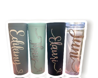 May include: Four personalized tumblers with names "Emily", "Trinity", "Eleanor", and "Sunny" in rhinestones. The tumblers are in various colors, including blue, green, and black.