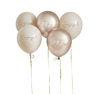 May include: A cluster of five round balloons in shades of cream and metallic champagne gold. Each balloon features the word Engaged printed in a cursive script font. Thin gold ribbons are attached to the base of each balloon for hanging.