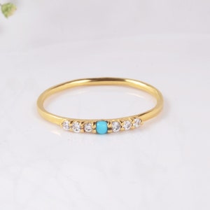 Op de afbeelding: Een delicate gouden ring met een turquoise edelsteen en kleine heldere stenen gezet in een band.