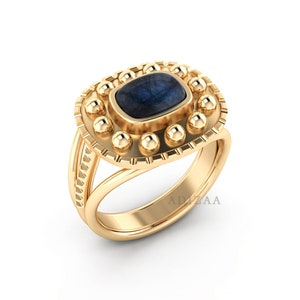 Puede incluir: Un anillo de oro con una piedra preciosa azul engastada en un engaste decorativo. El engaste está rodeado de pequeñas bolas de oro.