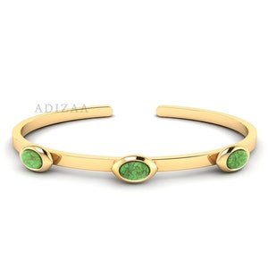 May include: A gold bangle bracelet with three oval-shaped green stones set into the band.