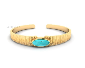 May include: A gold cuff bracelet with a textured finish and a turquoise oval stone set in the center.