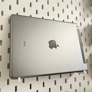 Op de afbeelding: Een zilveren iPad met het Apple-logo en de tekst "iPad" op de achterkant. De iPad is gemonteerd op een wit prikbord.