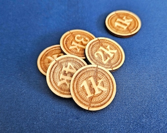 May include: Wooden game tokens with engraved numbers and the letter "K" are scattered on a blue surface. The tokens are circular, with a light brown color and a detailed, etched design around the edges. The numbers on the tokens are 1K, 2K, 3K, and 4K.