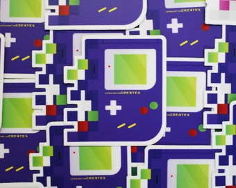 Könnte beinhalten: Nahaufnahme von mehreren violetten und weißen Aufklebern mit einem pixeligen Game-Konsolen-Design. Die Aufkleber zeigen einen grünen Bildschirm, ein rot-grünes Pixel-Design, ein gelbes Pluszeichen und den Text "#shopifycreates".