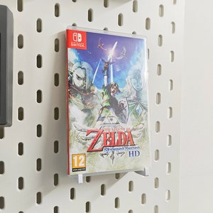 Puede incluir: Una caja de juego de Nintendo Switch con un diseño azul, verde y blanco. El juego es The Legend of Zelda: Skyward Sword HD. La caja tiene una clasificación de 12+ y es para mayores de 12 años.