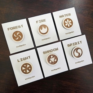 May include: Set of eight wooden pins with different symbols representing elements: Forest, Fire, Water, Spirit, Shadow, Light. Each pin has a white symbol on a brown background.