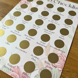 May include: A wedding checklist with gold circles to mark off tasks. The checklist includes items like "Book a Band/DJ", "Order Cake", "Plan the Decor", "Send Invitations", "Write Your Vows", and "Finalize Guest List".