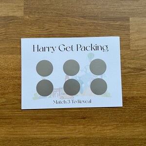 May include: A white card with the text "Harry Get Packing" and a colorful illustration of a travel scene. There are six gray circles on the card with the text "Match 3 To Reveal" at the bottom.