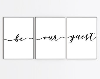 May include: Three black framed prints with white backgrounds. The prints are arranged horizontally and feature the text "be our guest" in black cursive.