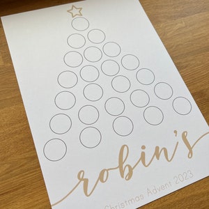 Peut inclure: Un calendrier de l'avent de Noël imprimable avec une étoile dorée et des cercles à remplir. Le texte "robin's Christmas Advent 2023" est en bas.