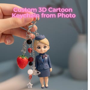 May include: A custom 3D cartoon keychain featuring a stewardess figurine in a blue uniform, a strawberry charm, and decorative beads. The keychain has a silver-colored clasp and chain. The text "Custom 3D Cartoon Keychain from Photo" is visible.