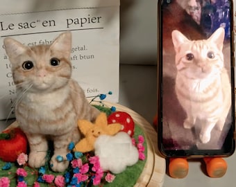 May include: A handmade ginger and white cat ornament with a detailed face, set on a green base with floral and felt decorations. A smartphone shows a matching cat image.