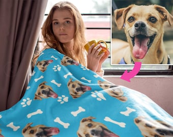 May include: A blue fleece blanket with a repeating pattern of white paw prints and bones. The blanket features multiple images of a dog's face.
