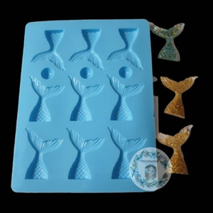 May include: A light blue silicone mold with nine mermaid tail shapes and three small round shapes. Several finished mermaid tail resin pieces in gold and teal glitter are displayed next to the mold. The mold has the text "MCboutiqueshop".
