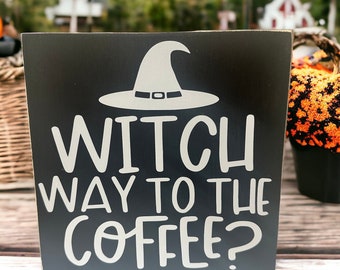 May include: Black wooden sign with white text and a witch's hat graphic. The text reads "Witch way to the coffee?"