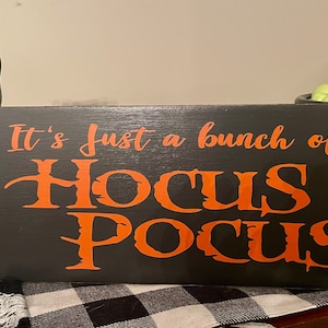 May include: Black wooden sign with the text "It's just a bunch of Hocus Pocus" in orange lettering.