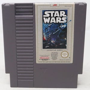 Op de afbeelding: Een grijze Nintendo Entertainment System spelcartridge voor Star Wars van JVC. Het label bevat het Star Wars logo, een X-wing starfighter in de ruimte en tekst waaronder Lucasfilm Games, Nintendo en Made in Japan. De cartridge heeft een geribbelde zijkant.